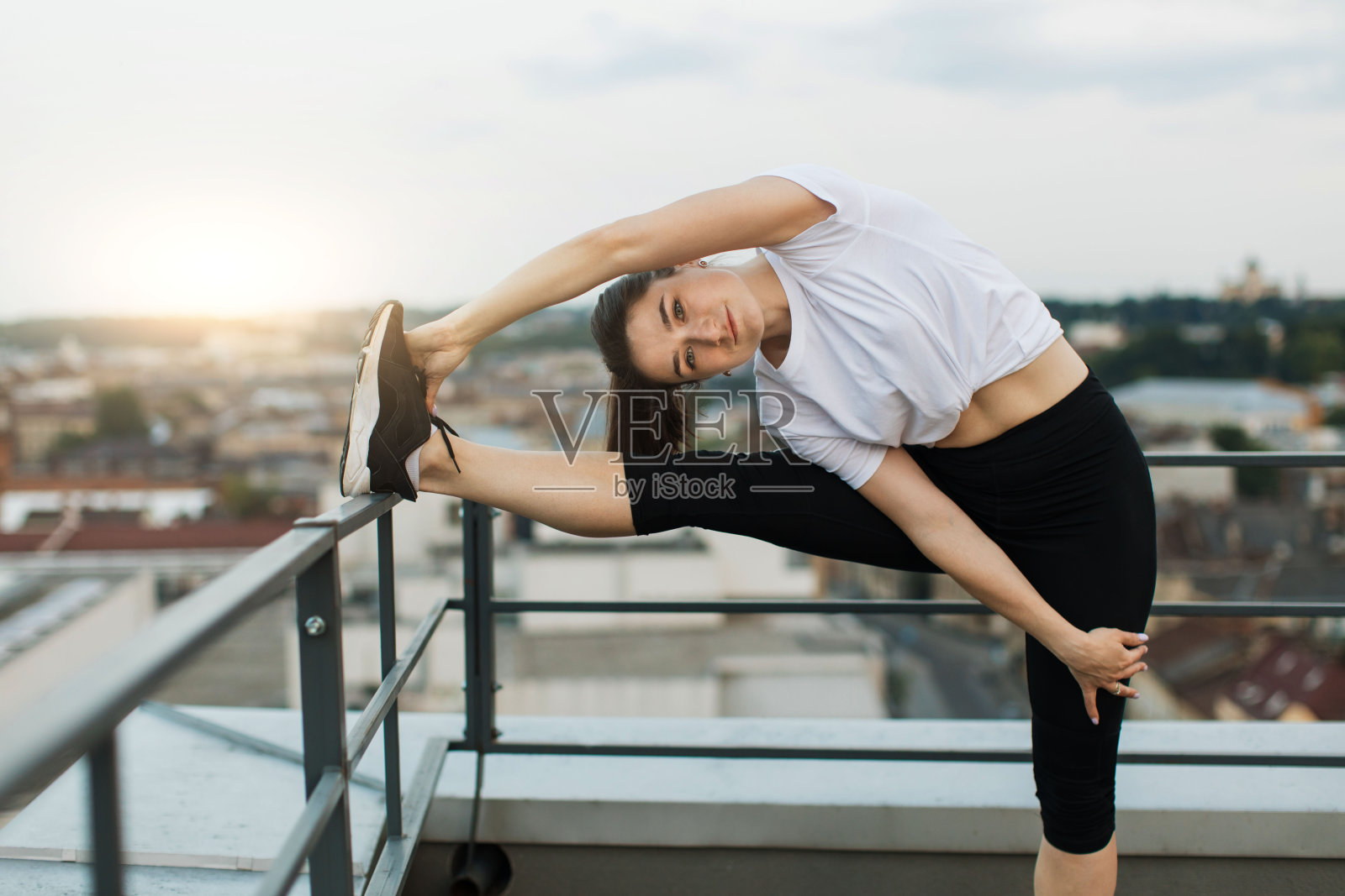 女性在傍晚的屋顶上锻炼时伸展肌肉照片摄影图片