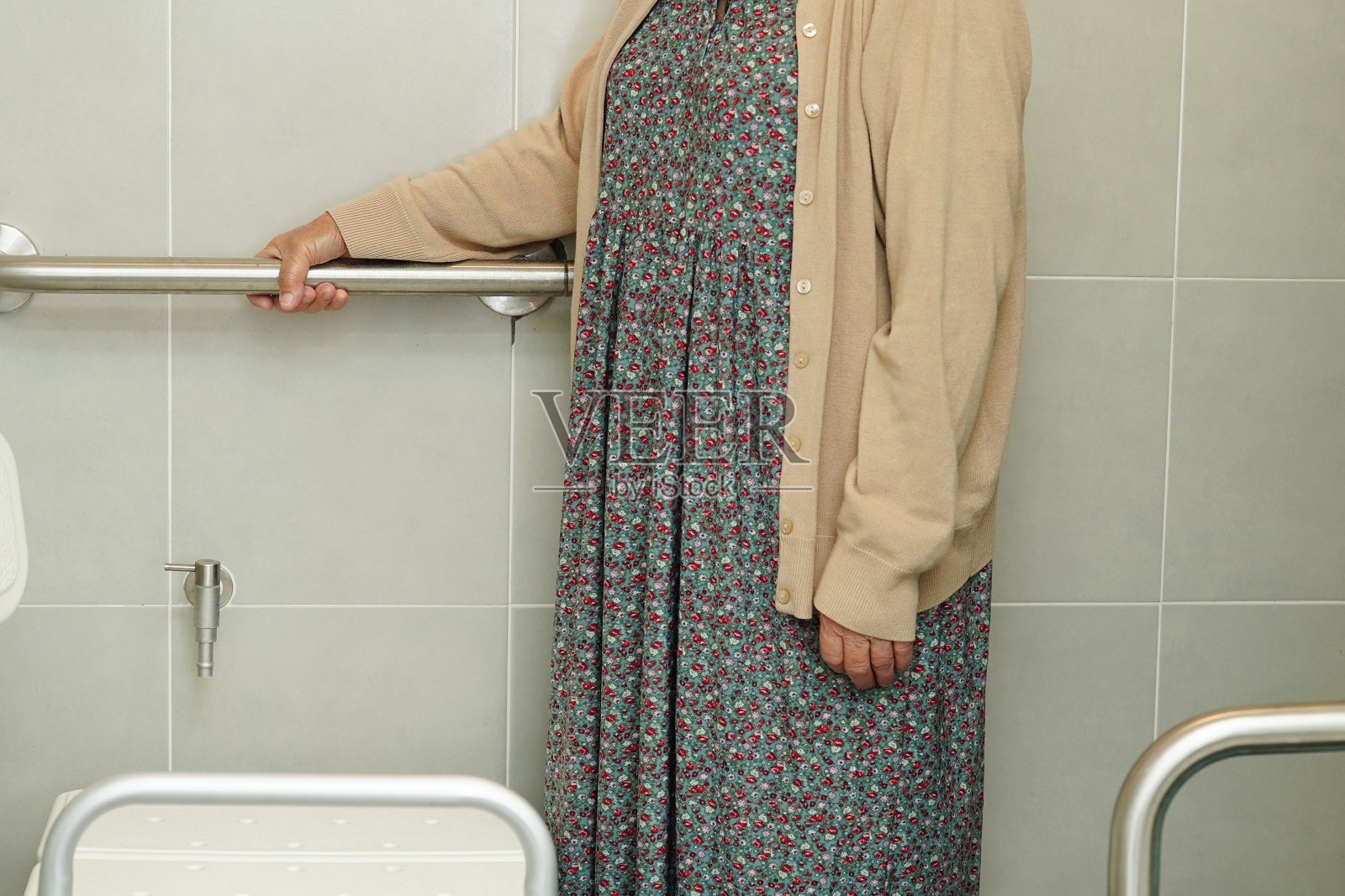 亚洲老年妇女患者在卫生间使用厕所托轨,在护理医院使用扶手安全抓杆。照片摄影图片