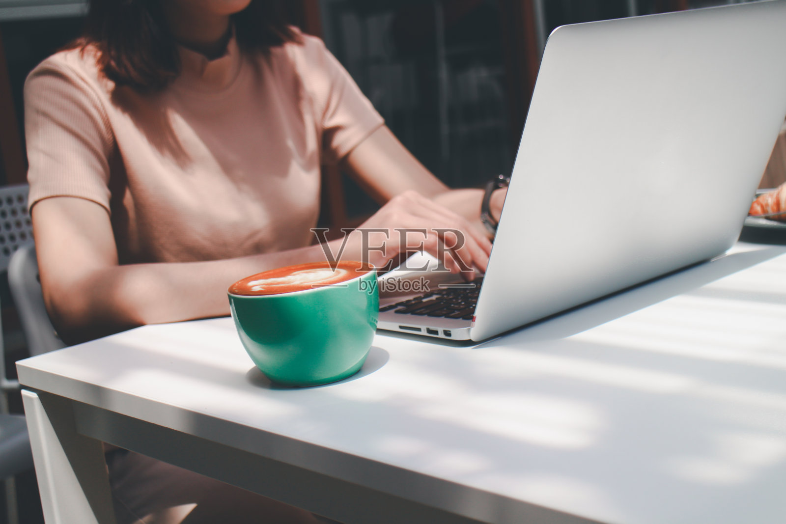 在咖啡馆里,一名女性拿着一杯拿铁咖啡和一块羊角面包,在笔记本电脑上工作照片摄影图片