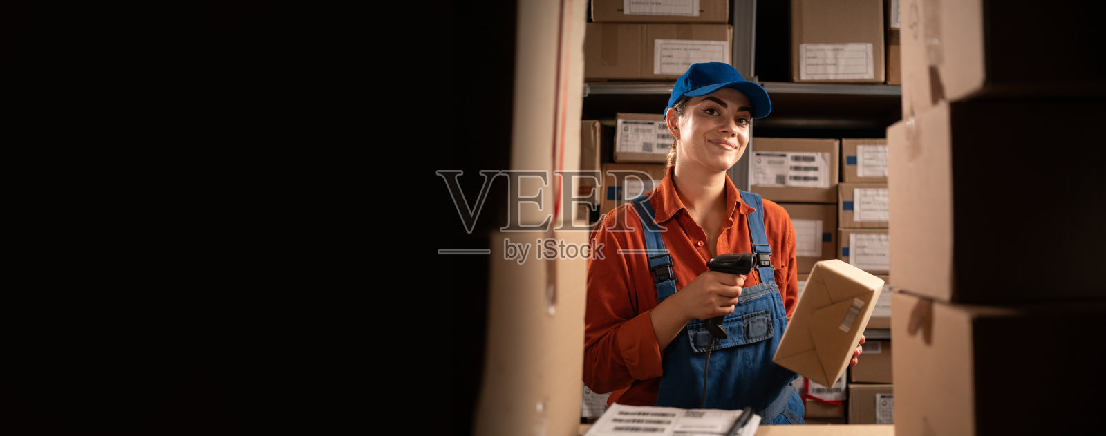 仓库存储技术概念。储存货物。仓库管理员的工作。穿工装裤的女人读着盒子上的条形码。本空间照片摄影图片