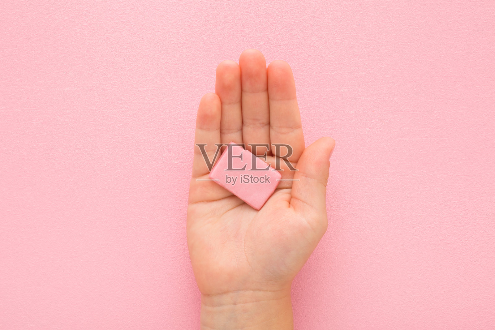 小女孩手拿着糖果口香糖垫,在浅粉色的桌子背景上。柔和的颜色。特写镜头。自顶向下视图。孩子的零食。照片摄影图片