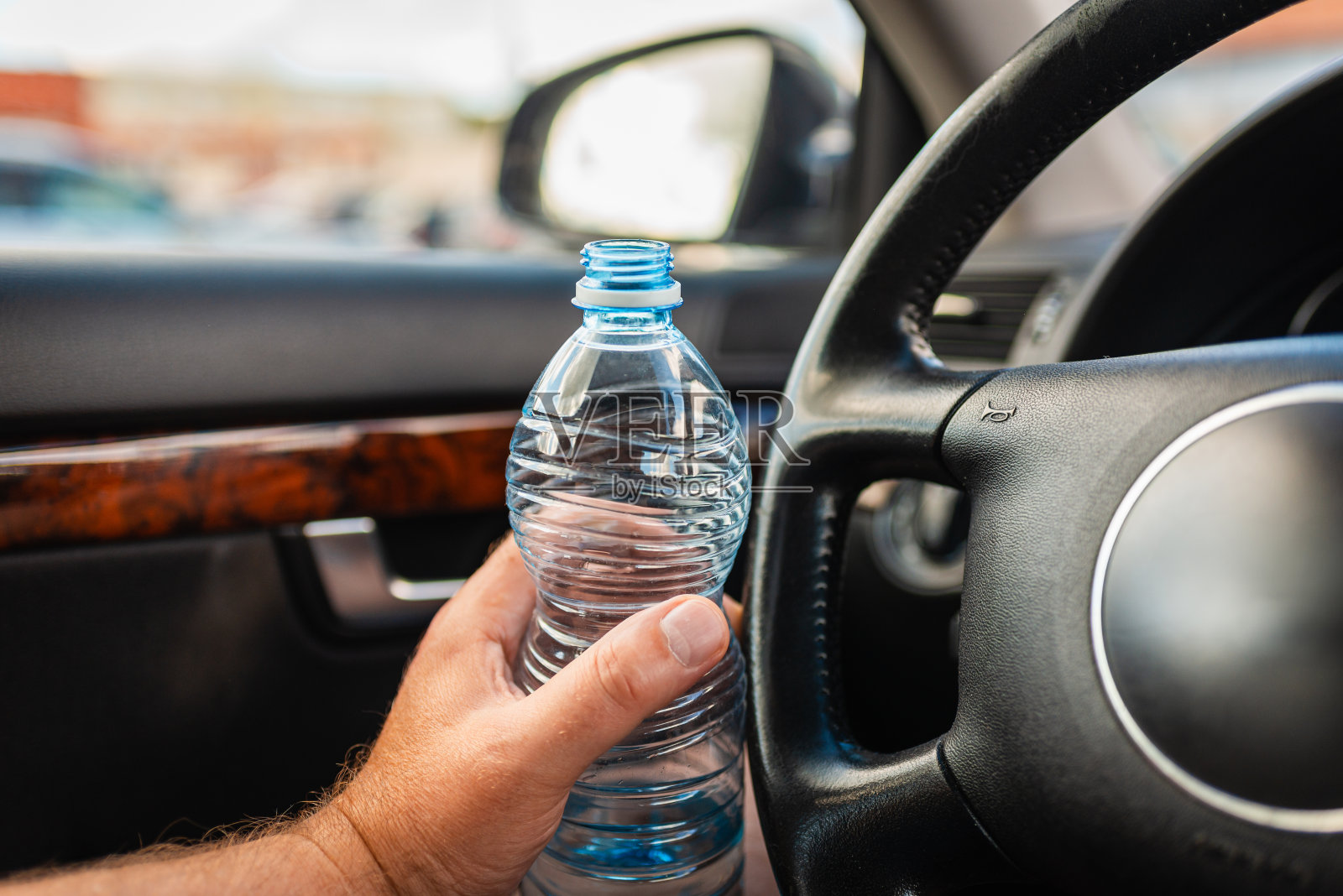 在交通中驾驶汽车时,男子手握塑料水瓶在车内。特写。照片摄影图片