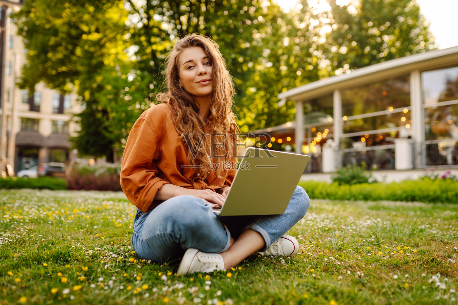 一位年轻女子坐在阳光明媚的公园空地上,用笔记本电脑工作。照片摄影图片