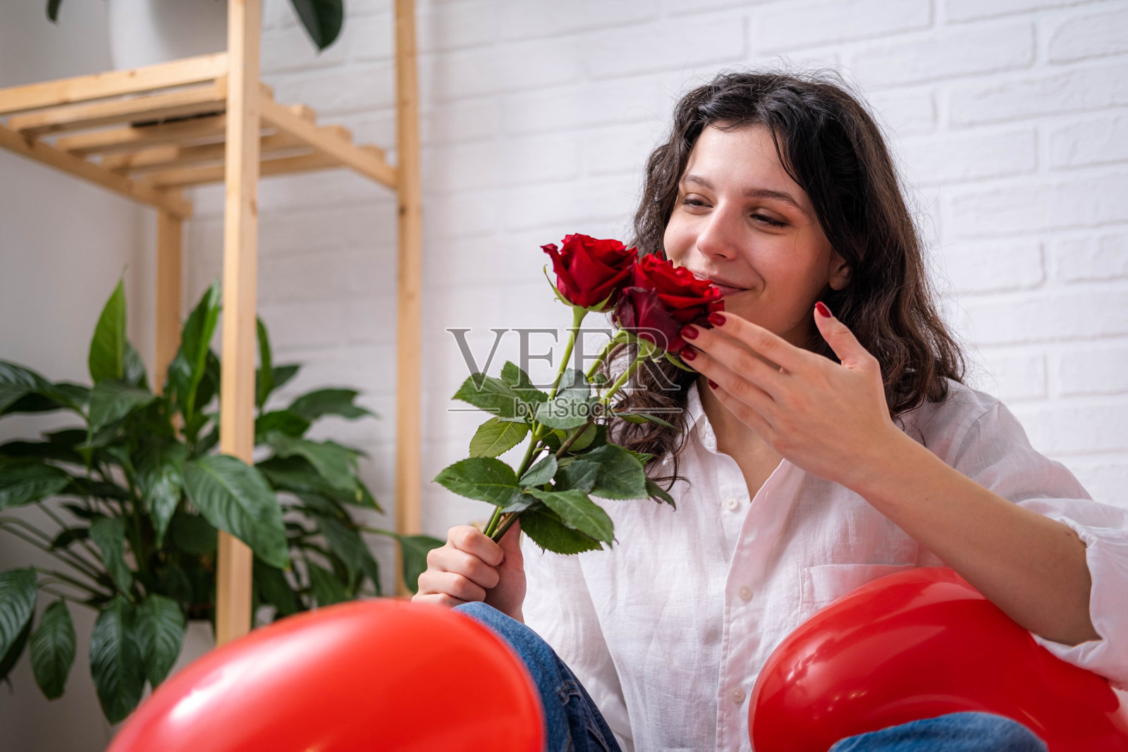 女孩在床上捧着一束玫瑰花,红色的心形气球。情人节,女人喜欢收到礼物。随和的长发女孩在情人节表达积极的情感照片摄影图片