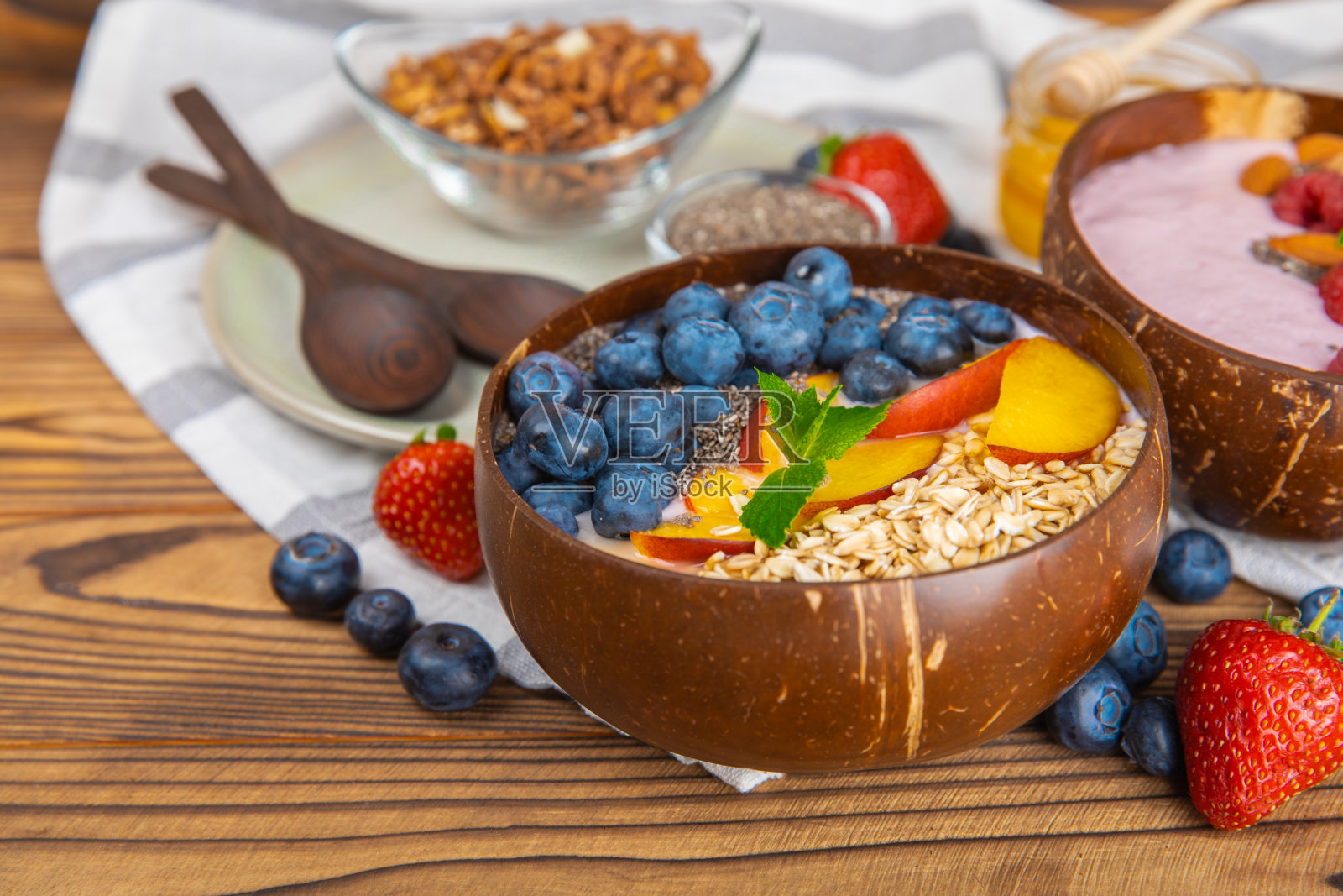 在厨房的桌子上,有一碗酸奶和新鲜的杏仁、蓝莓、覆盆子、桃子和草莓。巴西莓和螺旋藻碗。健康早餐概念。副本的空间。放文字的地方。照片摄影图片