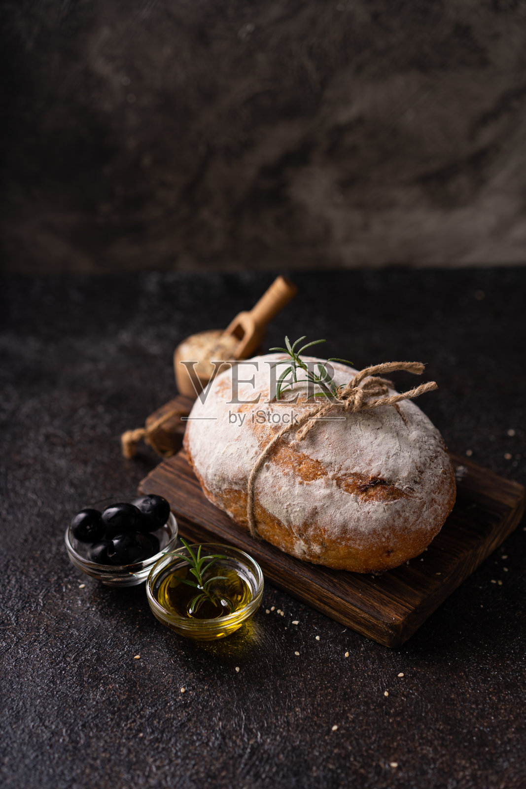 黑色质朴的桌子上,新鲜出炉的酸面包加橄榄和迷迭香。工匠面包照片摄影图片