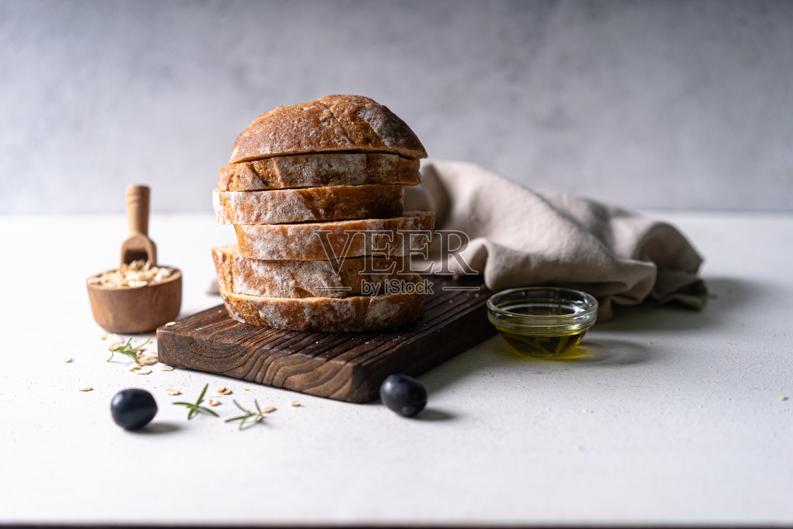 在一张白色抽象的桌子上,自制的酸面包、橄榄和迷迭香切片面包。工匠面包照片摄影图片