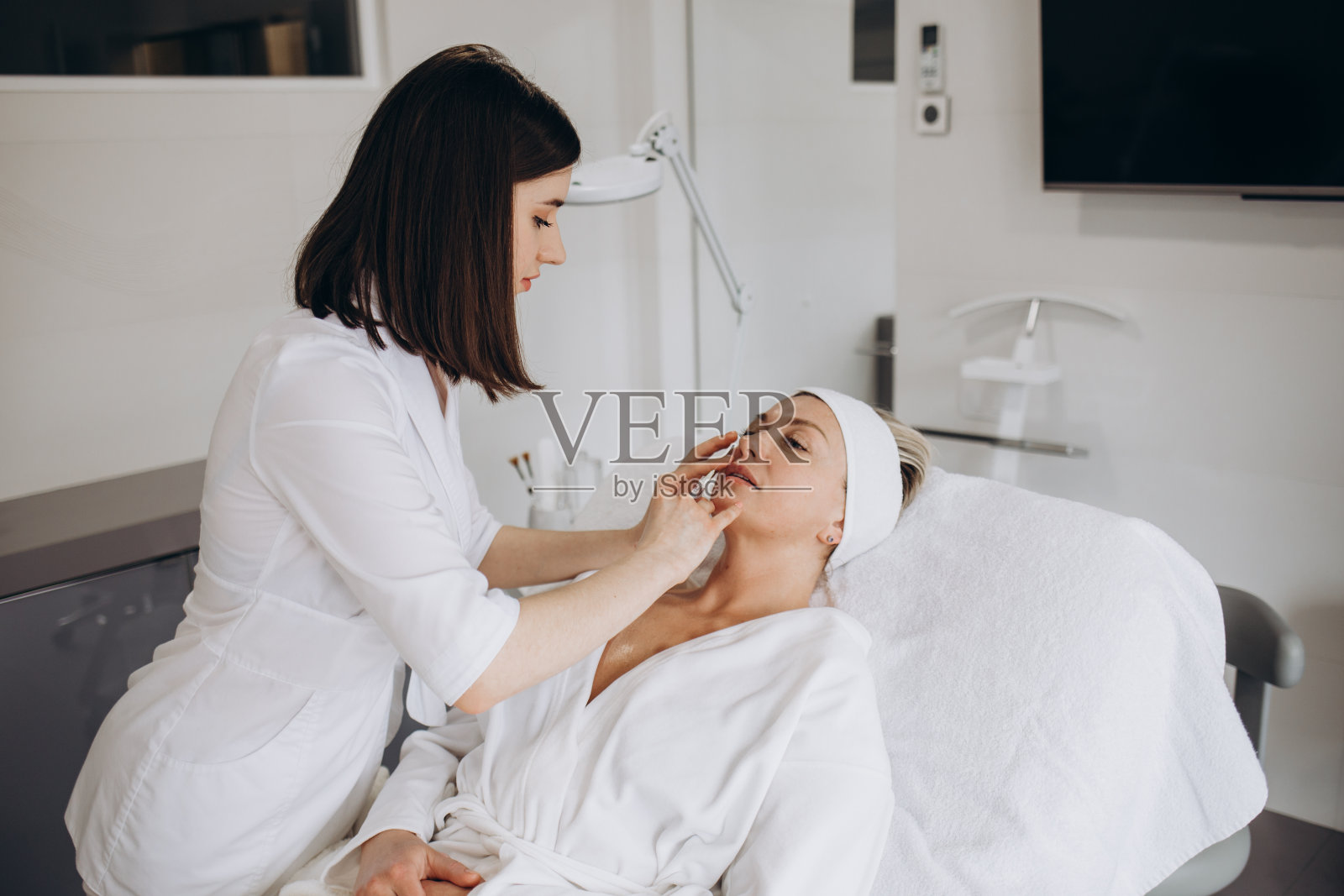 美容医生在美容院为一位美丽的年轻女子进行面部注射,以紧致和平滑面部皮肤上的皱纹。美容,护肤照片摄影图片