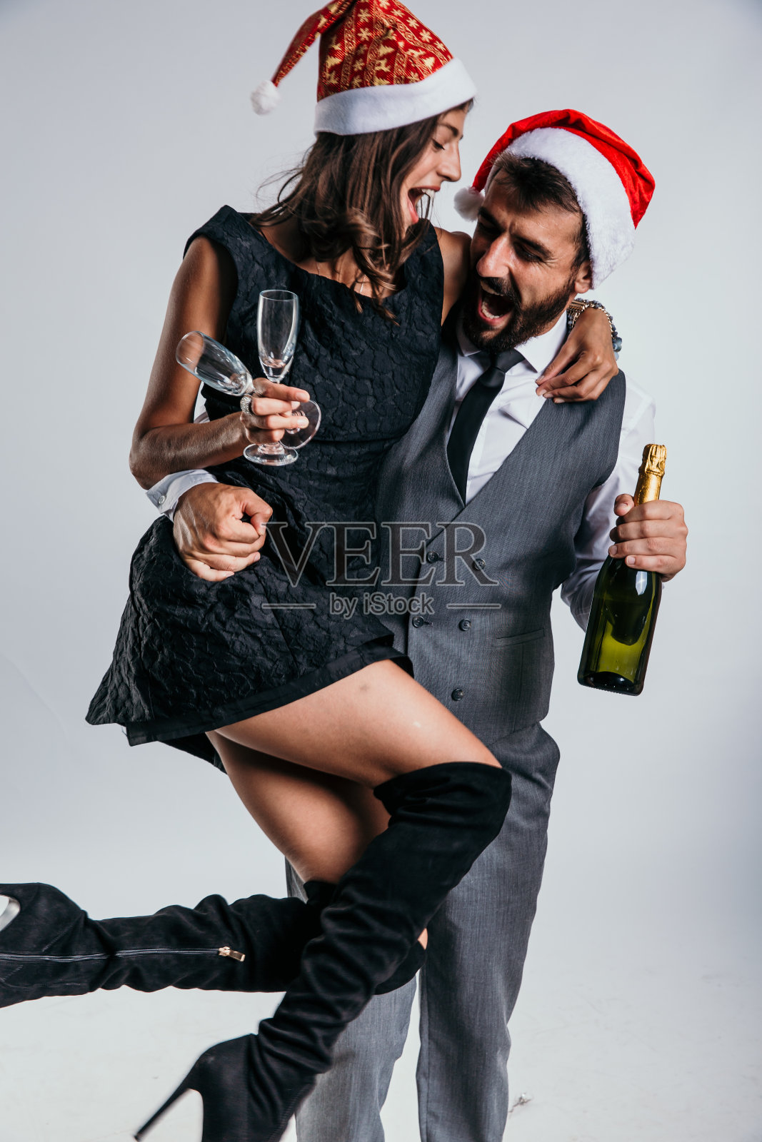 这对夫妇身着商务装,带着圣诞老人的帽子、酒瓶和酒杯,尽情享受着节日的气氛。照片摄影图片