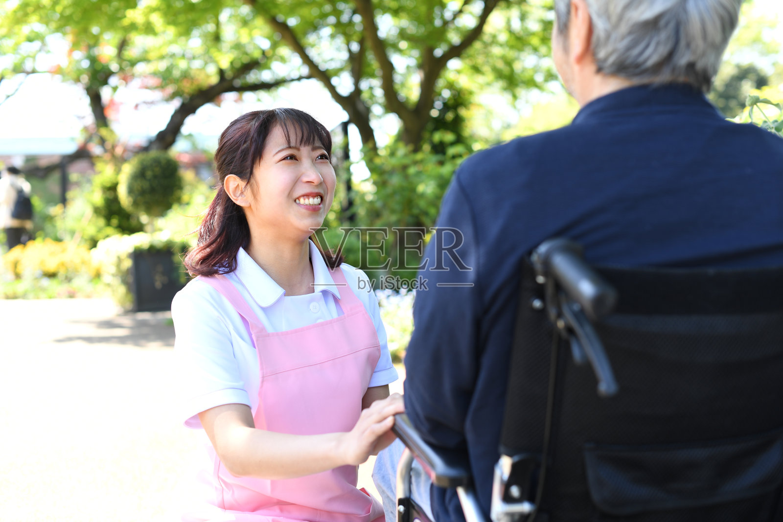 一位年轻的女护工微笑着与坐在轮椅上的一位白发苍苍的亚洲老人交谈照片摄影图片