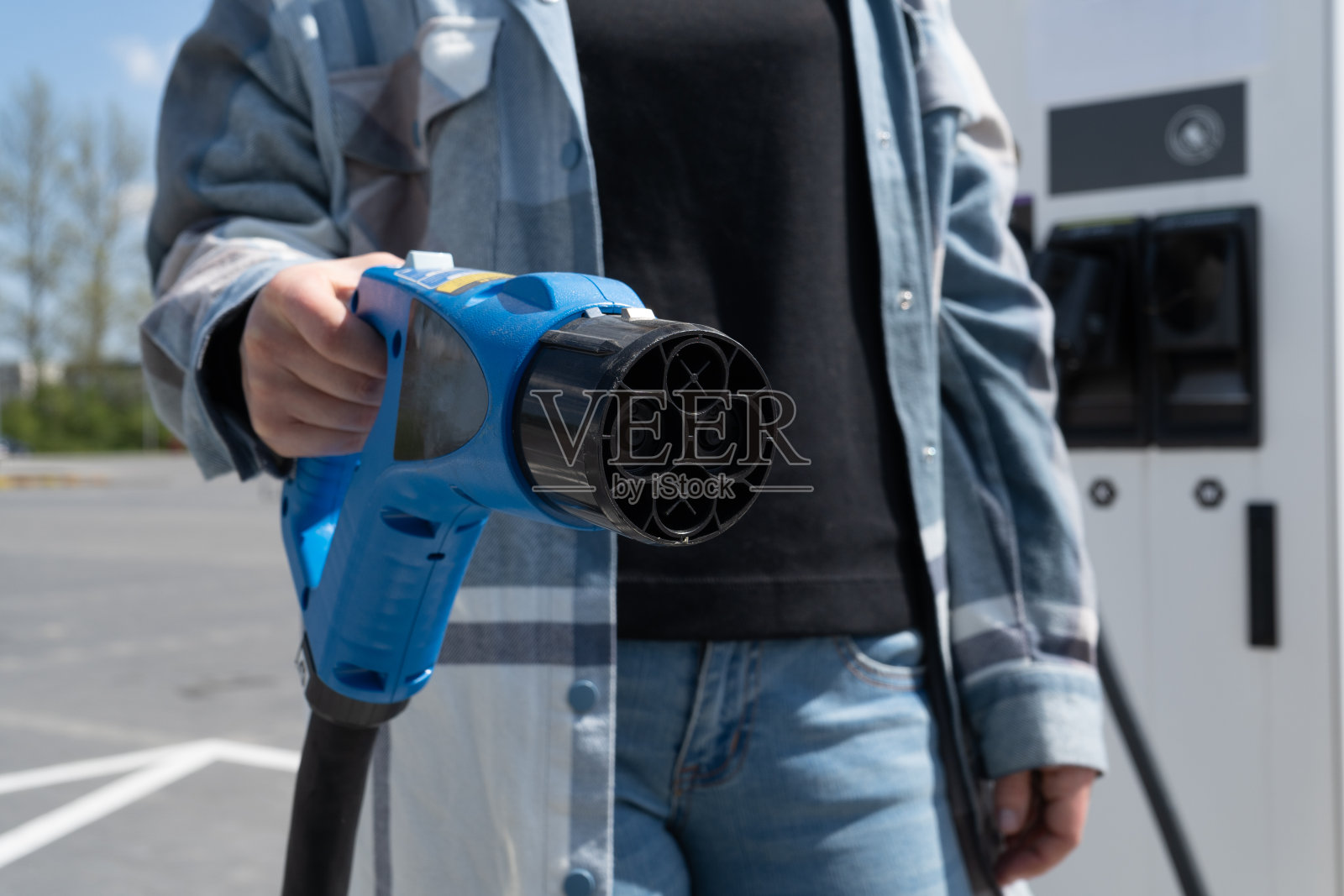 在电动汽车充电站,女子手持快速充电插座CHAdeMO插头。照片摄影图片