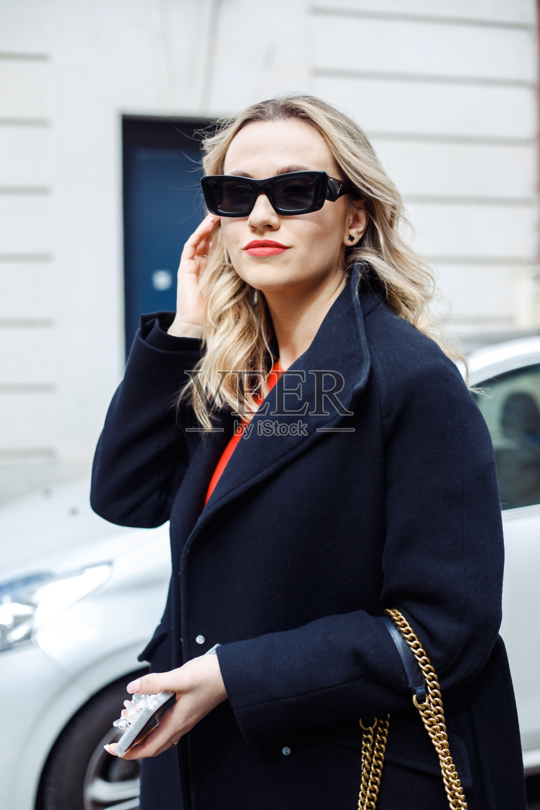 年轻自信的女商人站在大楼附近的街道上,拿着智能手机,带着链子的包。照片摄影图片