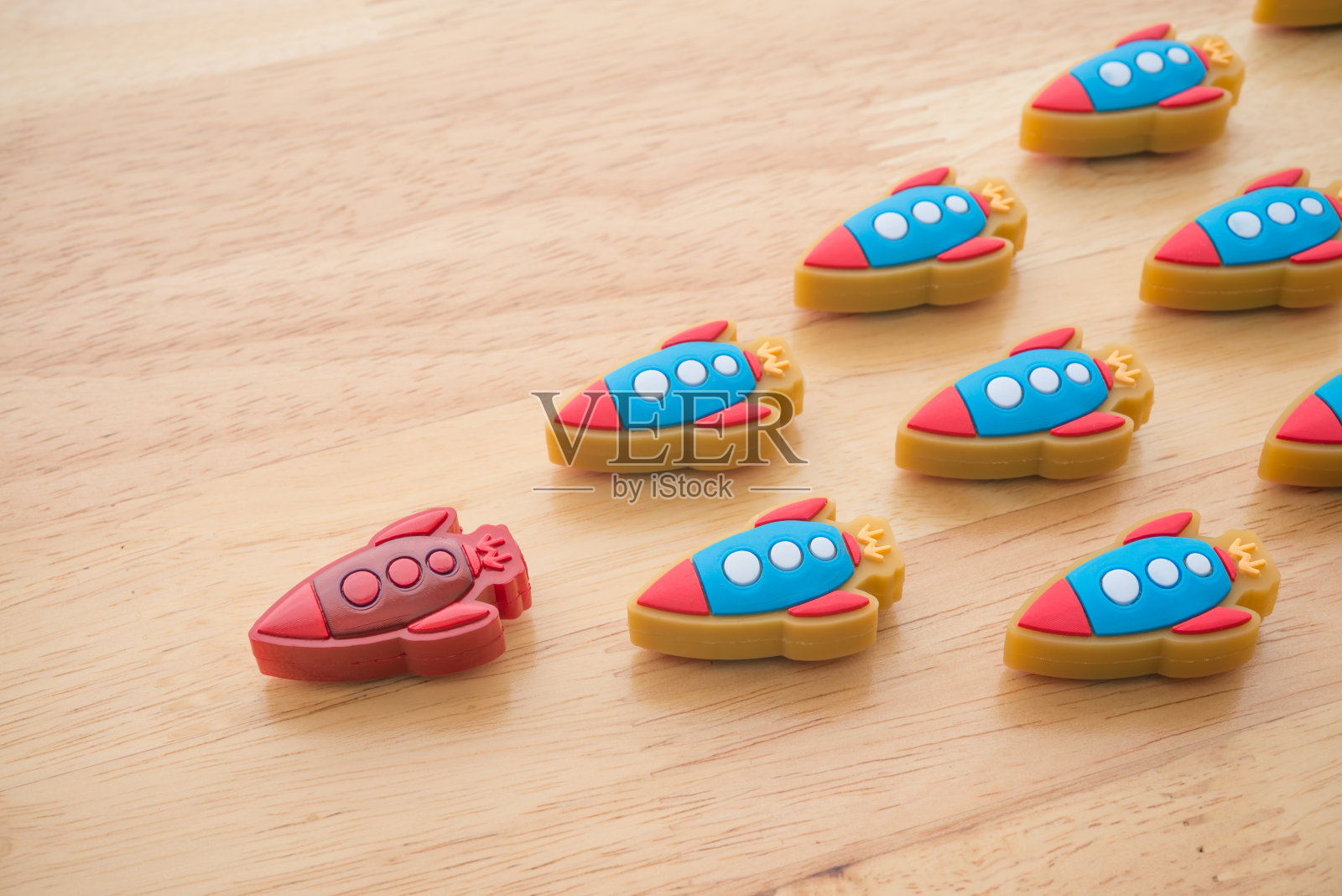 木制背景上,红色火箭在蓝色小火箭中间领先。照片摄影图片