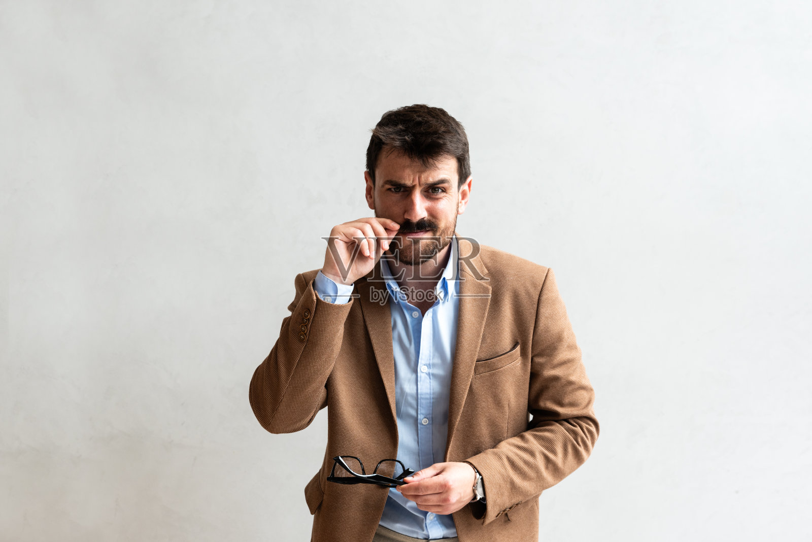 特写:微笑的年轻商人戴着眼镜做着鬼脸,看着镜头,背景是灰色的墙和复制空间。成功商务人士正装肖像照片摄影图片