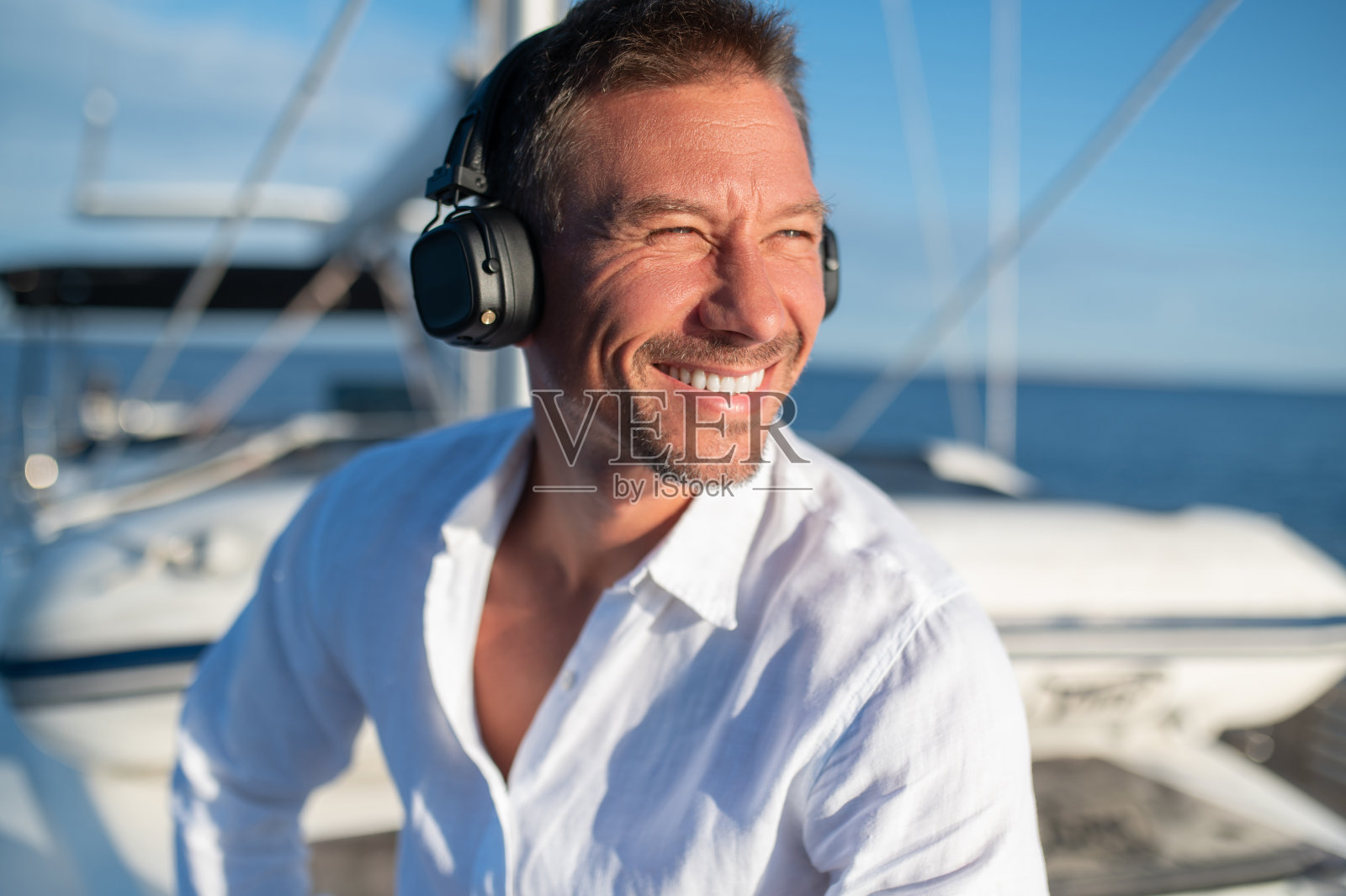 在游艇上航行时,戴着耳机听音乐的快乐男人照片摄影图片