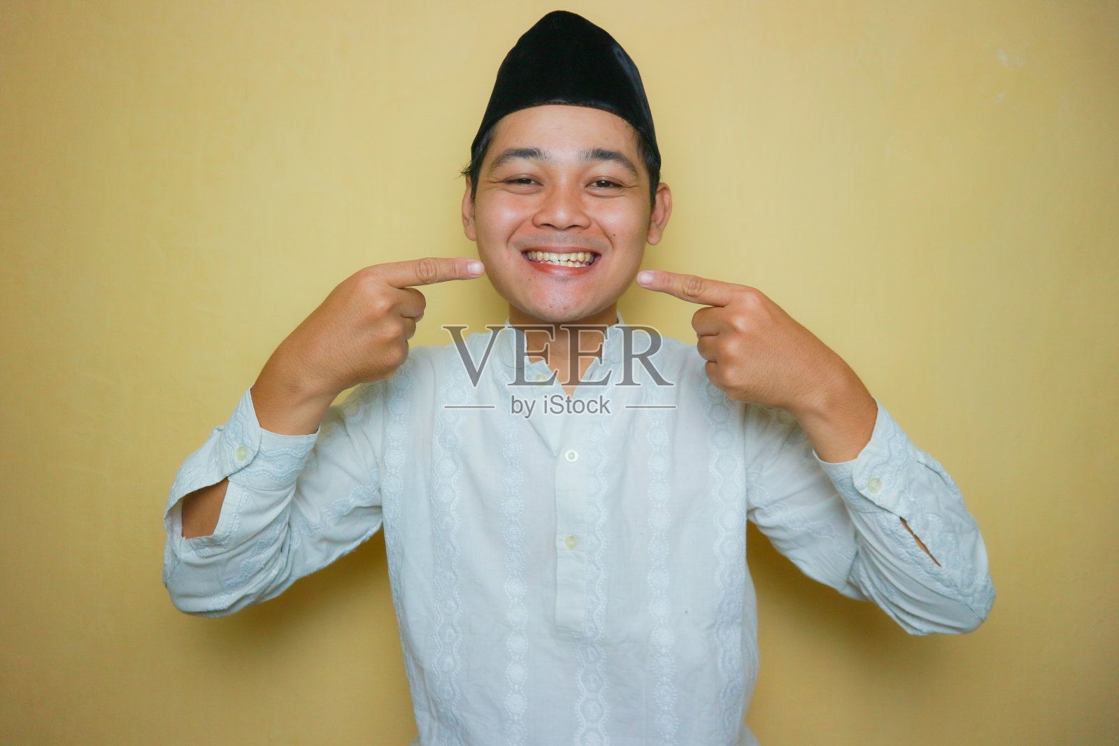 一名亚洲血统的印尼穆斯林男子,身穿穆斯林服装,头戴黑色胸围,庆祝宰牲节。孤立在黄色背景上,有着非常多样的表情照片摄影图片