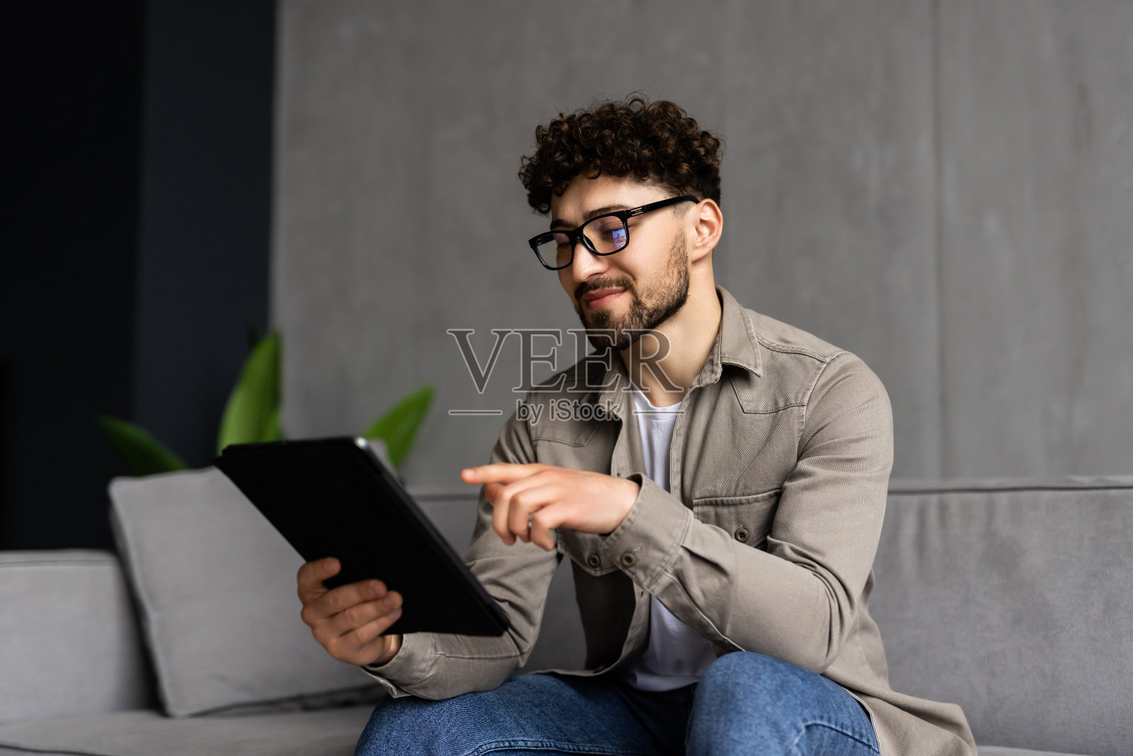 年轻英俊的男人在沙发上用平板电脑冲浪照片摄影图片