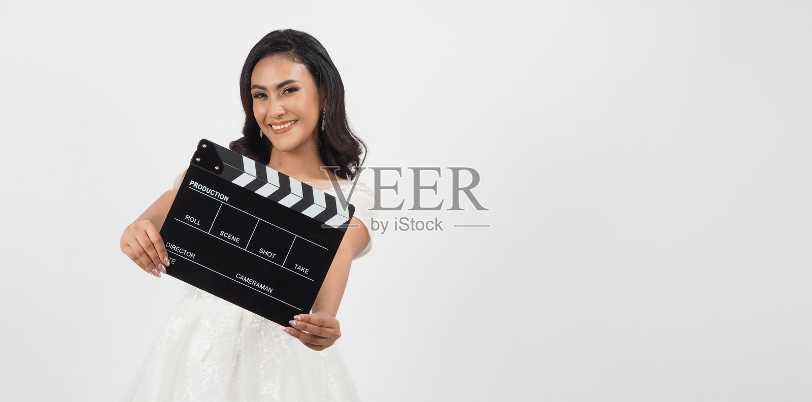 身着新娘礼服的女子手持白色背景的黑色拍板或电影板。照片摄影图片