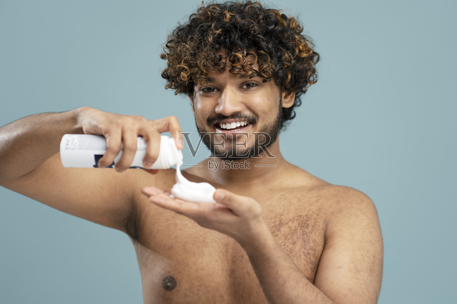 微笑的印度男子沐浴后赤裸上身,拿着剃须泡沫孤立在蓝色背景上照片摄影图片