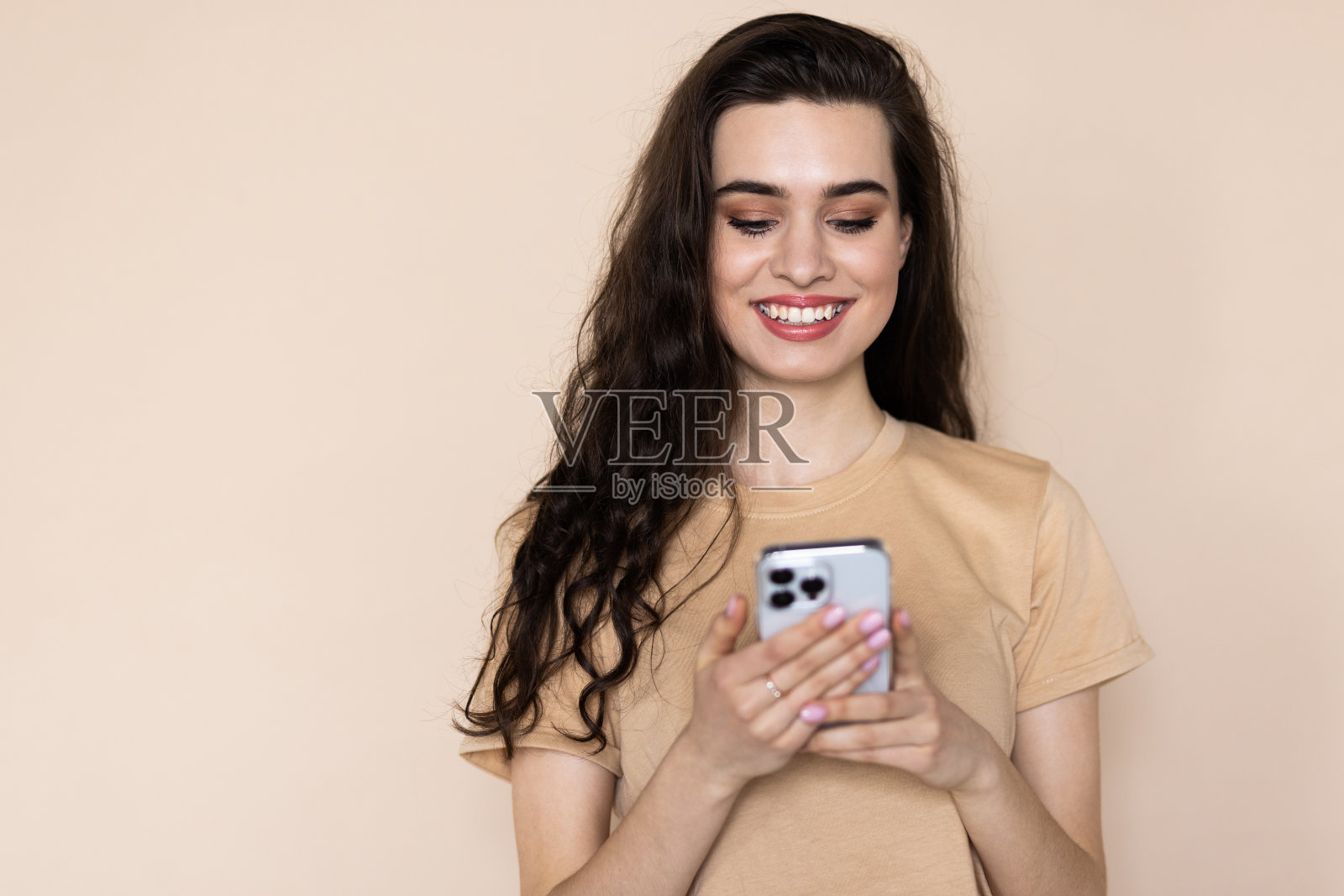 梦幻的女人拿着手机有沉思的表情想着收到的短信隔在米色的背景上。照片摄影图片