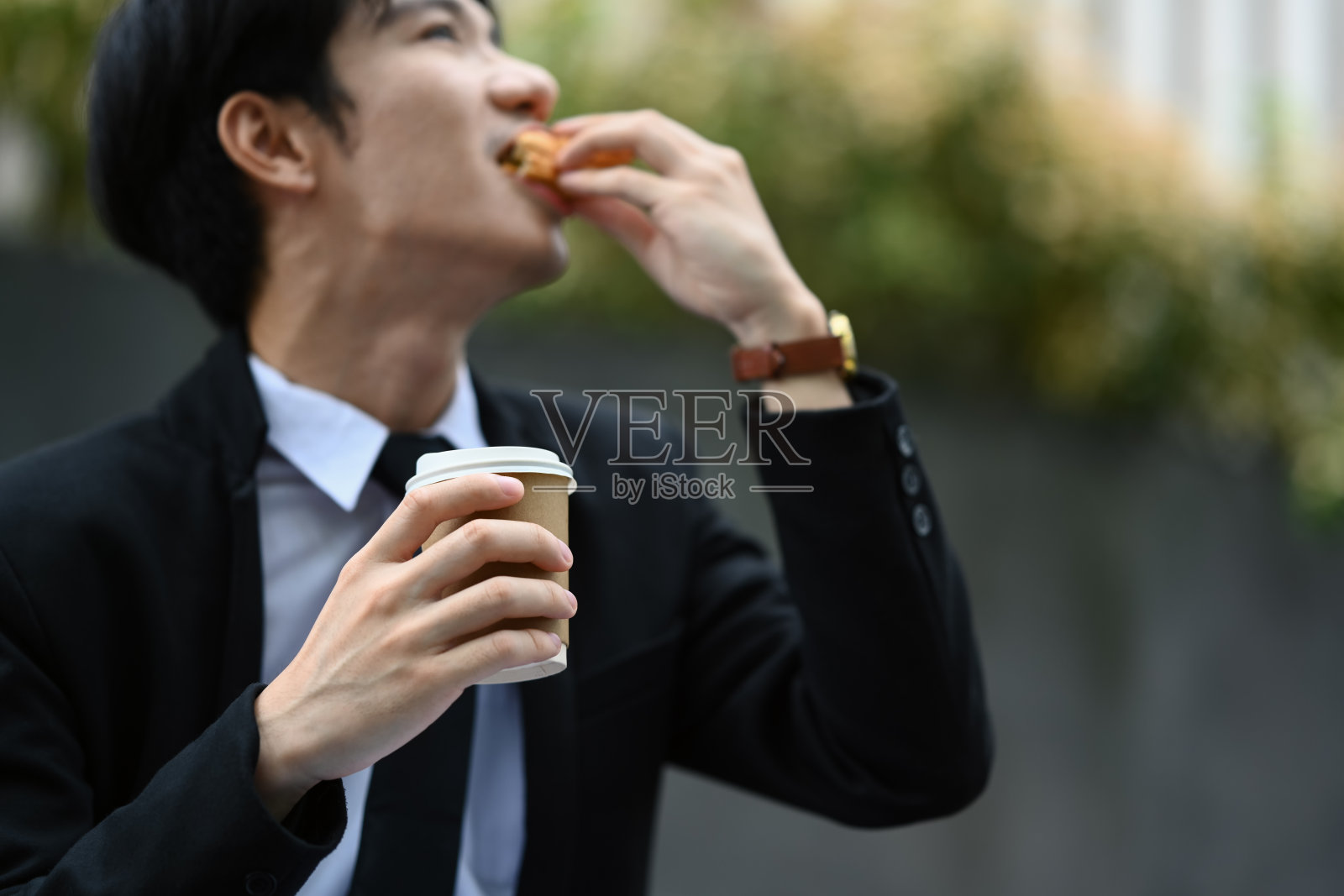 穿着正装的亚洲男性办公室职员坐在办公室外的楼梯上吃着美味的三明治照片摄影图片