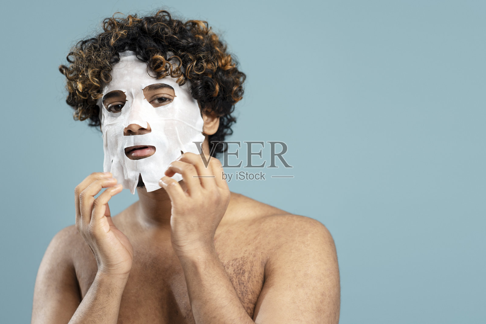 英俊的印度男子的肖像,他的脸上戴着面具,裸露的躯干孤立在蓝色背景上照片摄影图片