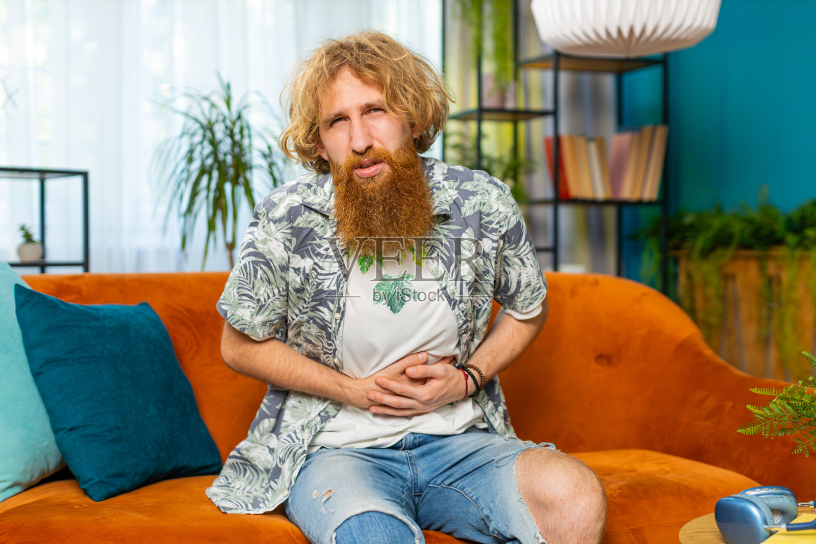 红发男子坐在沙发上突然感到腹胃痛、胃炎问题、腹泻照片摄影图片