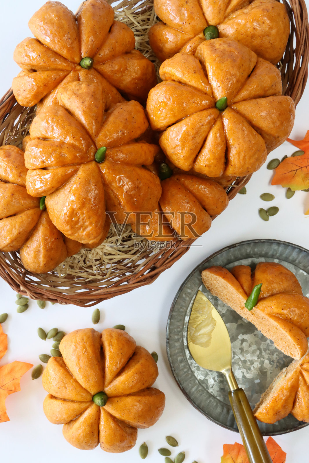 一堆南瓜设计的卷,柳条篮子里有绿辣椒梗,周围是南瓜子,半切和涂黄油的自制万圣节面包,盘子上涂着杏酱,白色大理石效果背景,高架视图照片摄影图片