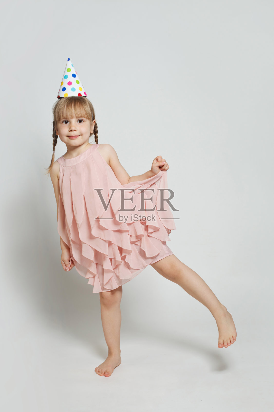 快乐、迷人、有趣的小女孩,戴着生日派对的帽子,在白色背景上摆姿势照片摄影图片