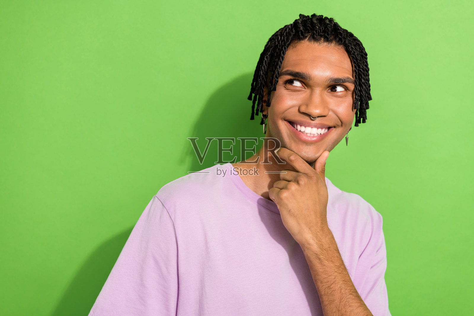 照片中开朗梦幻的小伙子穿着粉红色的t恤,手臂下巴看起来空荡荡,孤立的绿色背景照片摄影图片