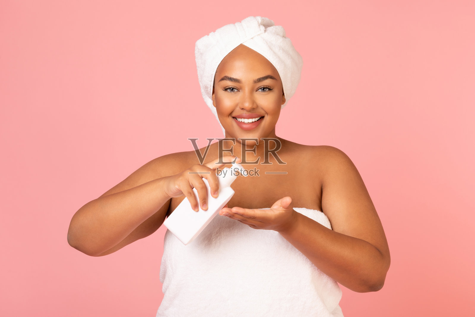 超重的非裔美国妇女拿着化妆品瓶在粉红色的背景照片摄影图片