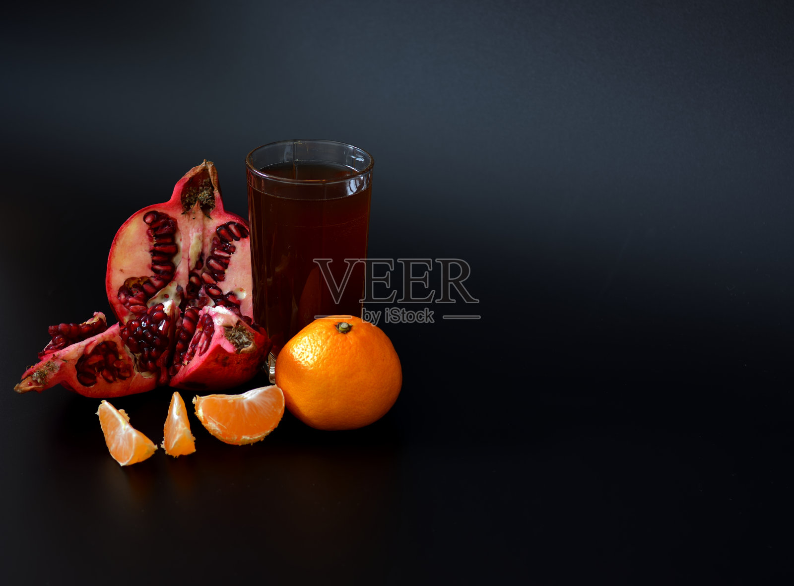 一大杯黑色背景的果汁,旁边是几片橘子和一个带籽的石榴碎。照片摄影图片