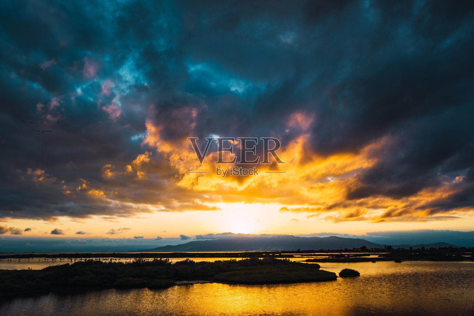 美丽的日落,太阳的球体在泻湖上空的云层之间的地平线上。照片摄影图片