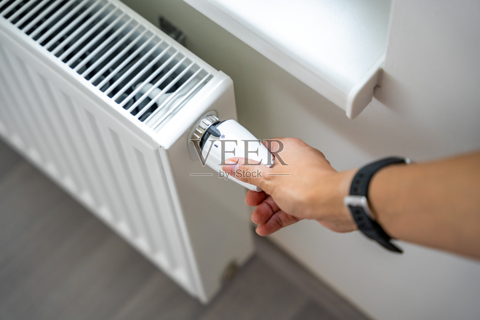 一个女人的手在转动电池加热旋钮。在家里的公寓里供暖。供热价格。照片摄影图片
