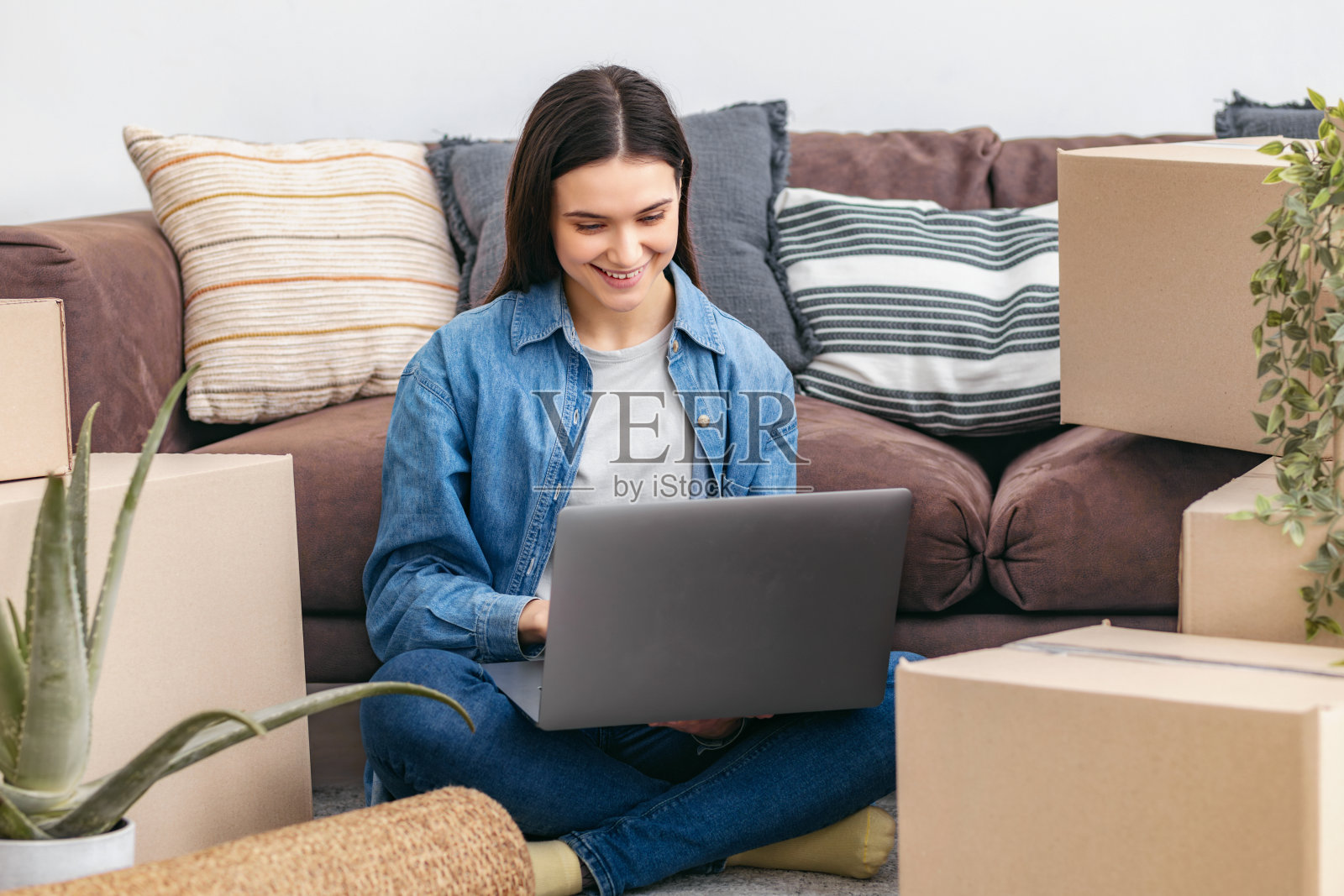 一个女人搬她的第一个新家时,坐在沙发旁边的地板上照片摄影图片