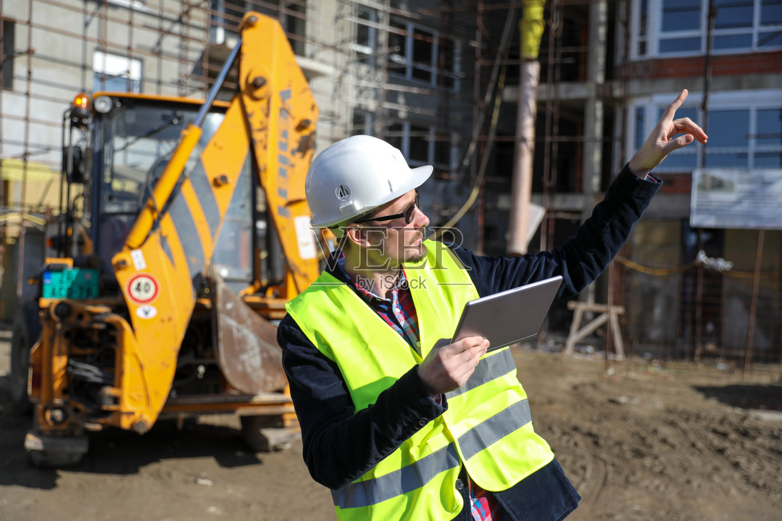 男建筑师在工地使用数码平板电脑,他穿着防护背心和头盔照片摄影图片