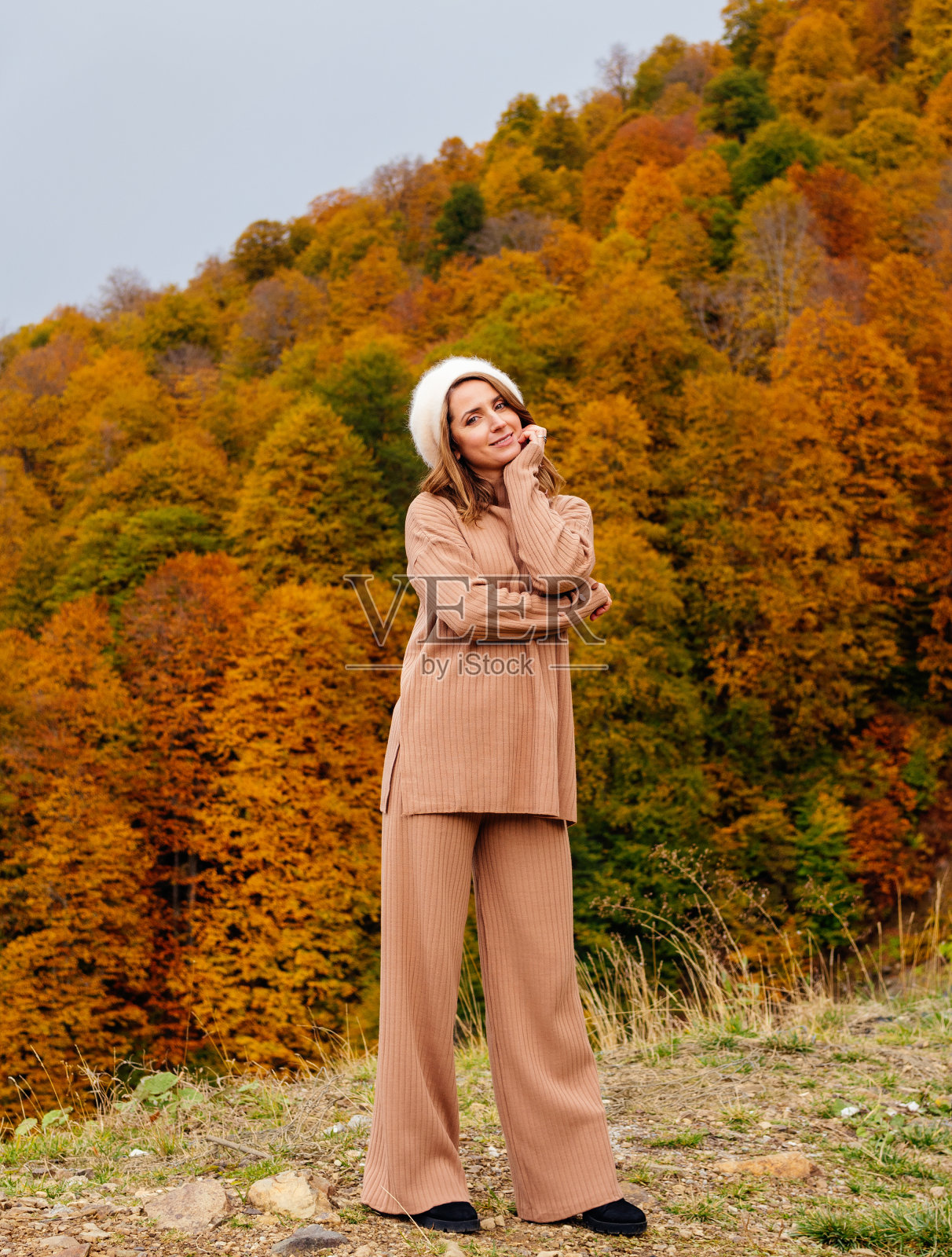 美丽的微笑的女人在米色的罗纹西装和贝雷帽的背景下,秋天的森林在山区。没有整形手术,没有修饰照片摄影图片