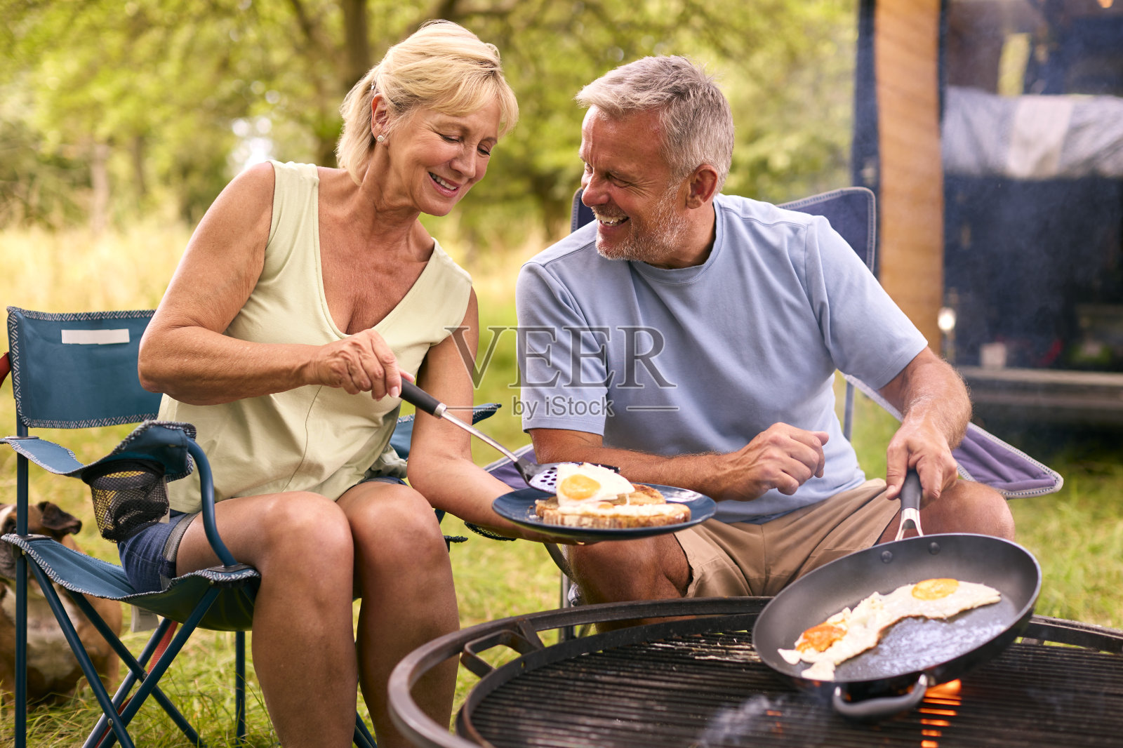 一对老年夫妇开着房车在乡下露营,用火在户外烤熏肉和鸡蛋做早餐照片摄影图片