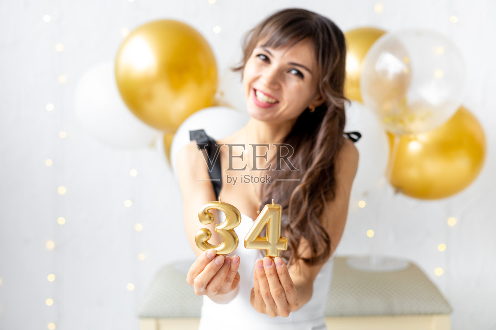 一个快乐的女孩在她的生日上拿着数字34 34的蜡烛,在白色的背景上享受着节日。照片摄影图片