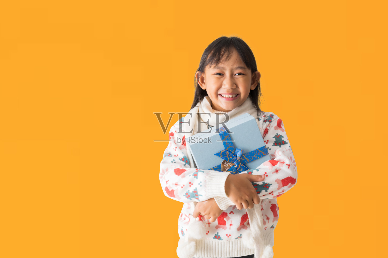 欢快快乐的亚洲小女孩的肖像,穿着圣诞毛衣服装,双手拿着圣诞礼盒祝新年快乐,孤立在黄色背景上照片摄影图片