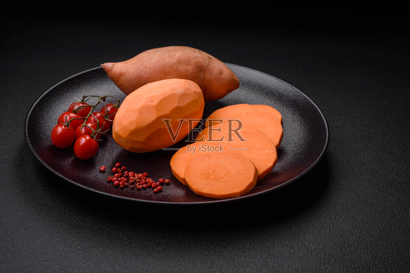 新鲜的粉色大红薯块茎,配以西红柿和香料,背景为深色照片摄影图片