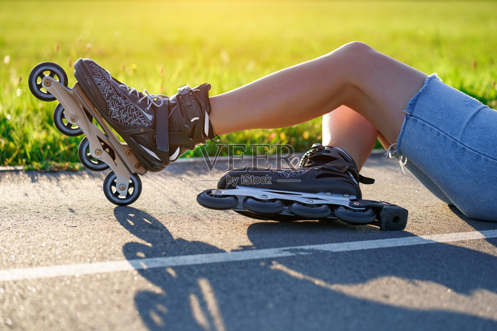 一名女子滑旱冰时跌倒在柏油路上。没有保护的直排滑冰。轮滑时受伤和擦伤照片摄影图片