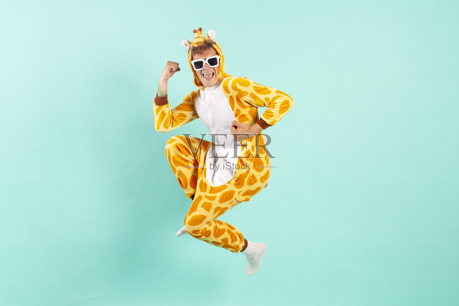 穿着橙色长颈鹿睡衣的搞笑小哥在派对上跳起来,戴着墨镜庆祝成功照片摄影图片