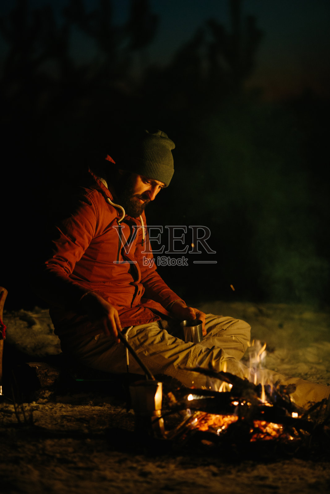 冬天的森林里,一个留着胡子的年轻人在夜间营火旁休息。野外生存和徒步旅行的概念。照片摄影图片