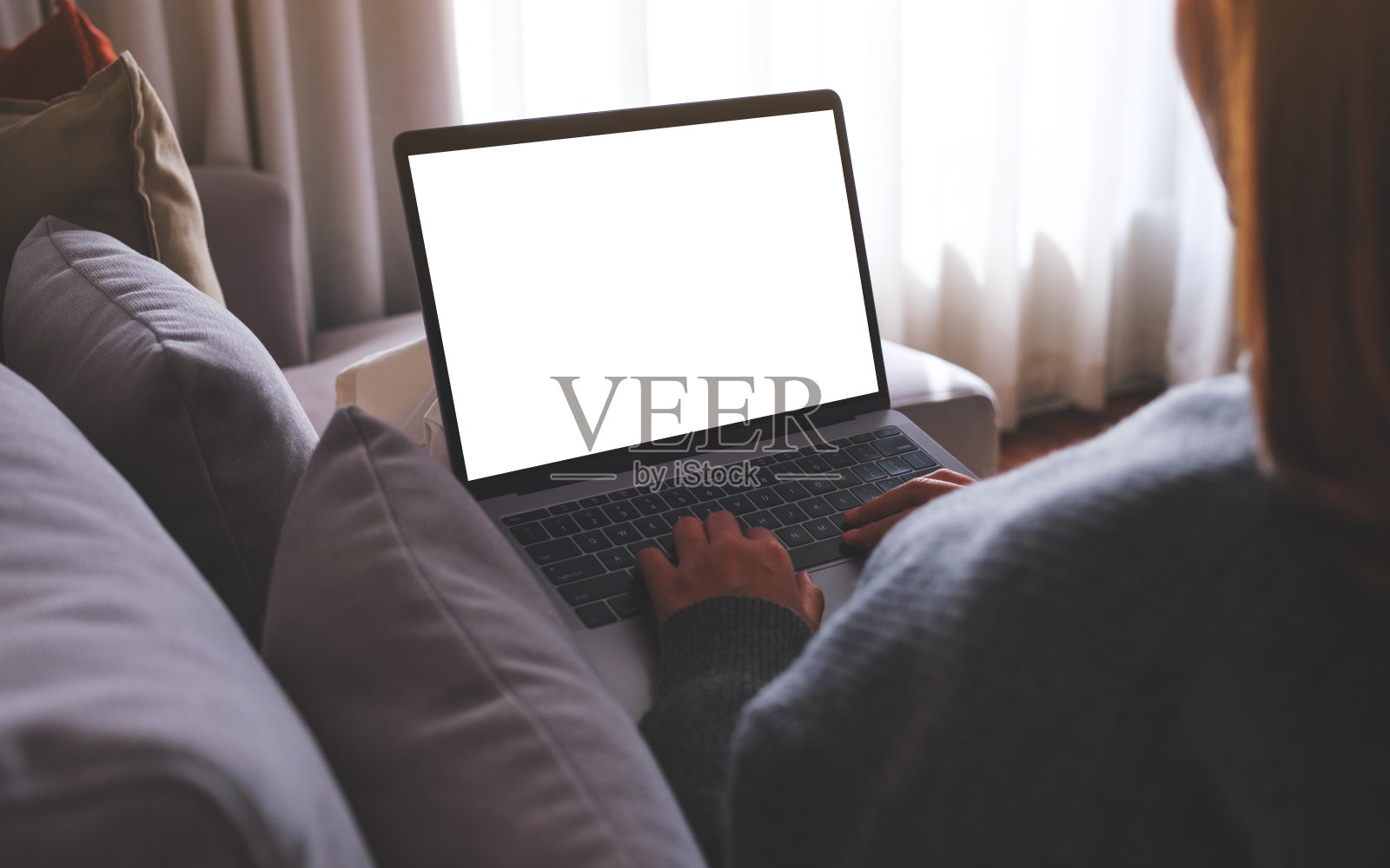 一个女人坐在家里的沙发上,在空白屏幕的笔记本电脑上工作和打字的模拟图像照片摄影图片