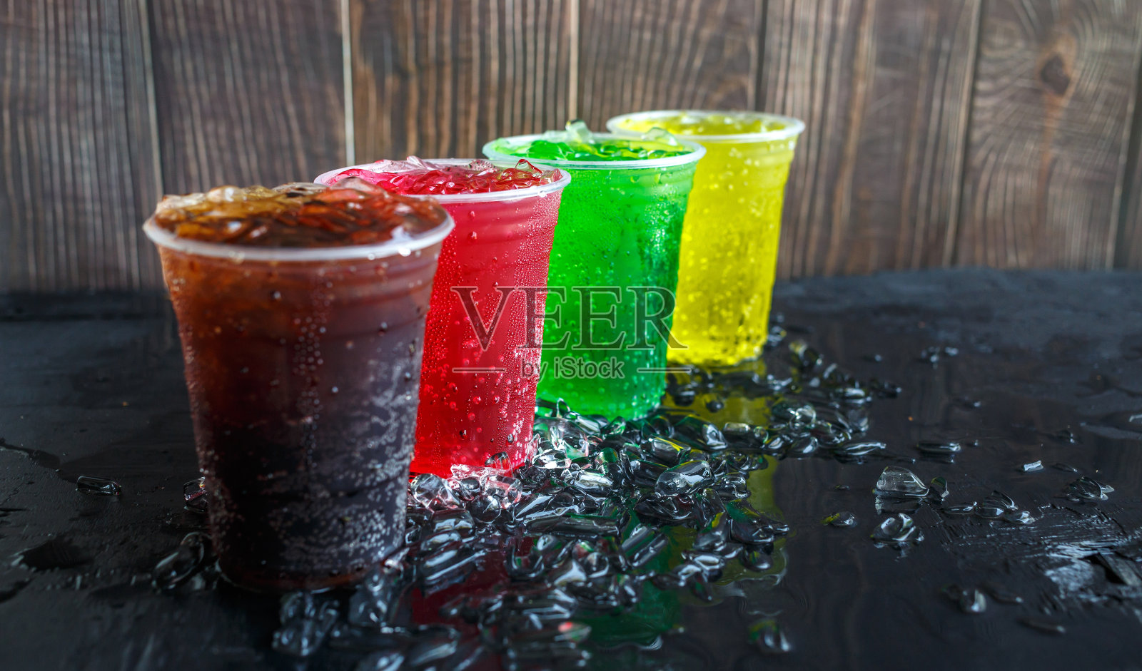 很多软饮都是装在彩色的、有味道的塑料杯里,里面有冰块,黑色的背景是冰块,软饮或碳酸饮料都是加冰的照片摄影图片