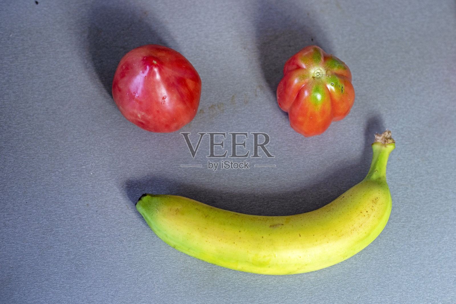 灰色的桌面上放着香蕉和自制的红色西红柿。flatlay照片摄影图片