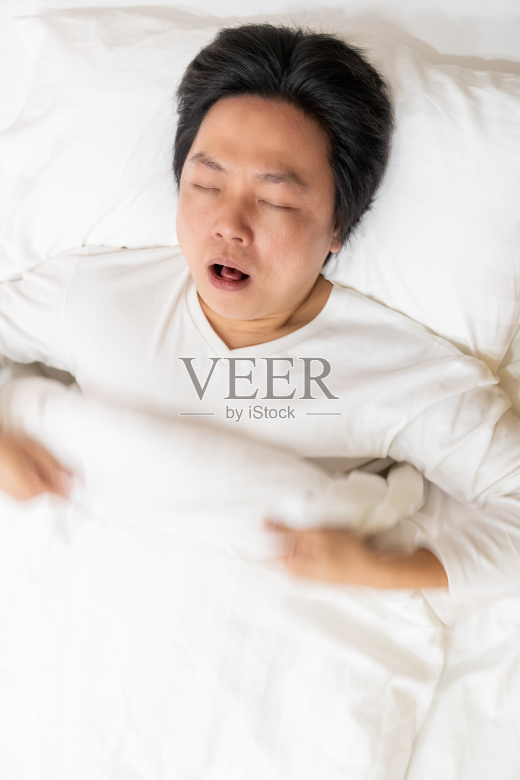 俯视图的亚洲年轻人在白色睡衣有慢性咳嗽和喉咙痛,而晚上睡在床上。照片摄影图片