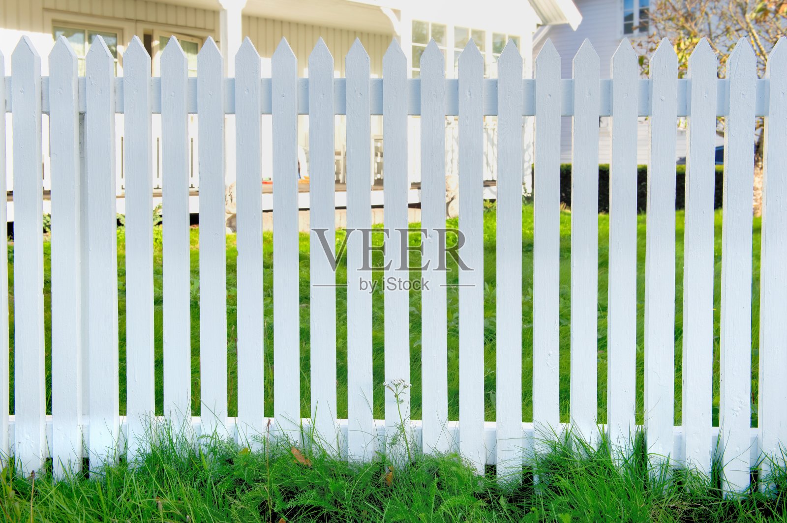 白色木制花园的栅栏,正面有绿色的草地和部分房屋背景照片摄影图片