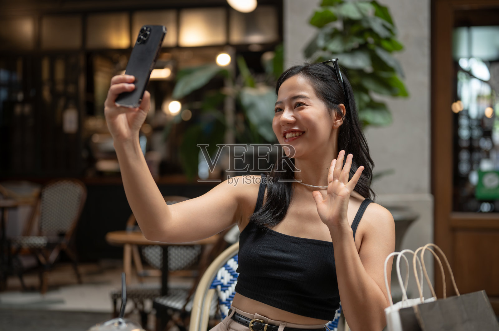 一位快乐的亚洲女性在咖啡馆放松时正在用她的智能手机自拍。照片摄影图片